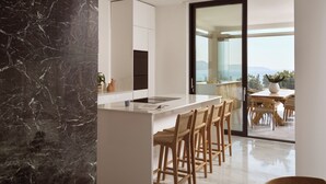 Una cocina moderna con salpicadero de mármol, una isla central con taburetes de bar y vistas al exterior a través de una puerta corrediza de vidrio.