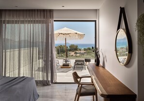 Ein Schlafzimmer mit großem Fenster, einem Bett, einem Schreibtisch, einem Stuhl und Meerblick.