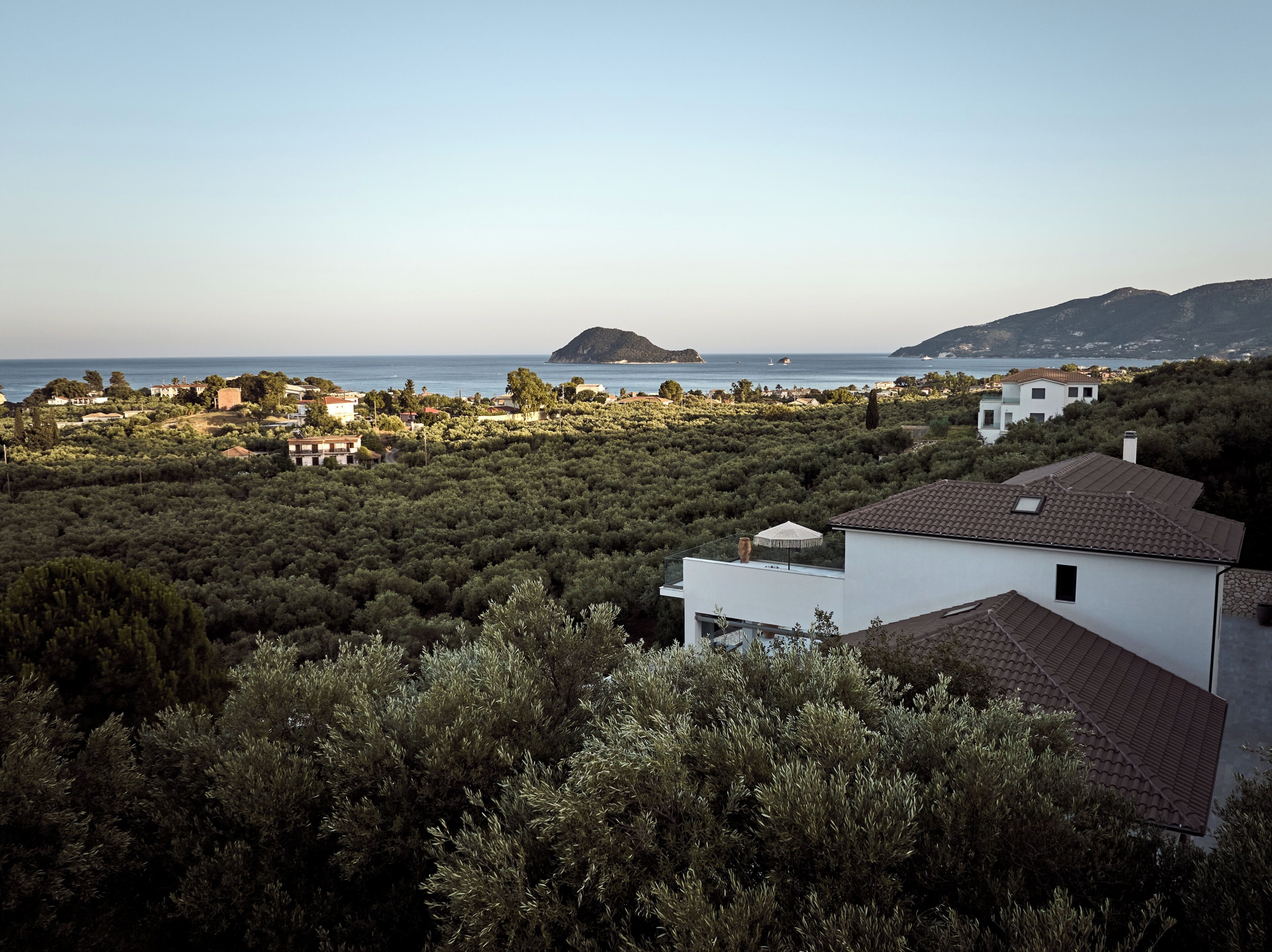 A coastal residential area with houses, dense vegetation, and a view of the sea.