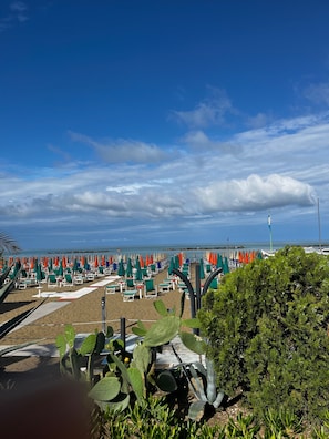 Ein Strand mit Reihen von Liegestühlen und Sonnenschirmen, einem klaren Himmel und einem entfernten Blick auf eine Brücke.