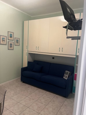 Ein Zimmer mit einem blauen Sofa, einem weißen Schrank mit türkis Knöpfen und einem Deckenventilator.