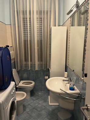 A bathroom with a washing machine, two toilets, a sink, and a shower curtain. - Casa Brisol Riviera delle Palme – Cozy Apartment Steps from the Beach (San Benedetto del Tronto)
