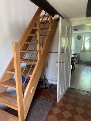 Eine Holztreppe mit Metallgeländern führt zu einem Raum, der eine weiße Tür, eine Heizung und einen Schachbrettboden hat.