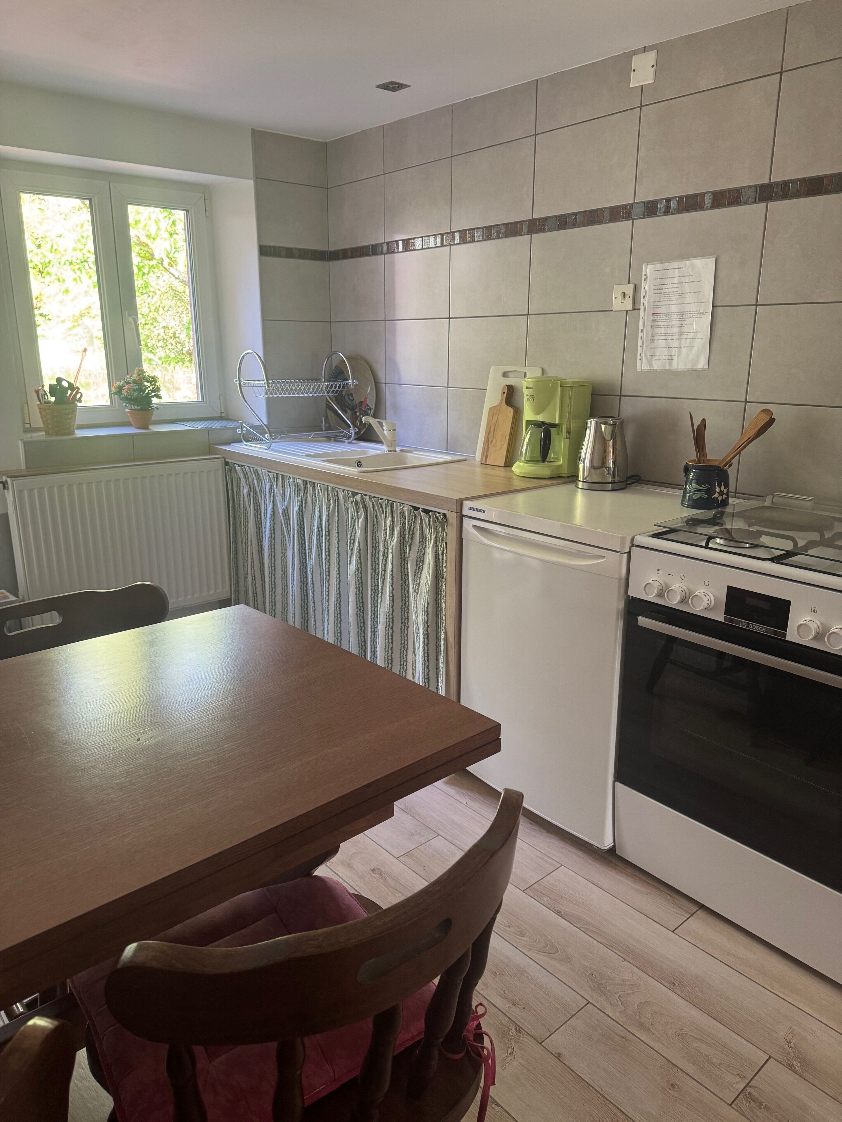 Una cocina con una mesa de madera, un lavamanos, un horno Bosch y una ventana con plantas.