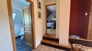 Ein Flur mit einer Holztür, die zu einem Badezimmer, einer Treppe und einem Schlafzimmer mit Bett und Nachttisch führt.