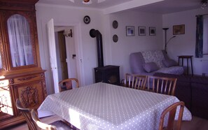 A dining area with a table covered in a polka dot tablecloth, wooden chairs, a vintage wooden cabinet, and a black stove.