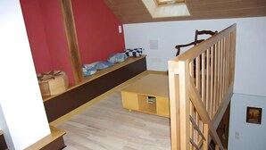 Ett rum med en säng på ett loft, ett litet bord, en bänk och ett träräcke.