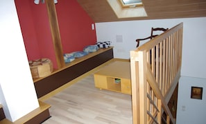 A room with a loft bed, a small table, a bench, and a wooden railing.