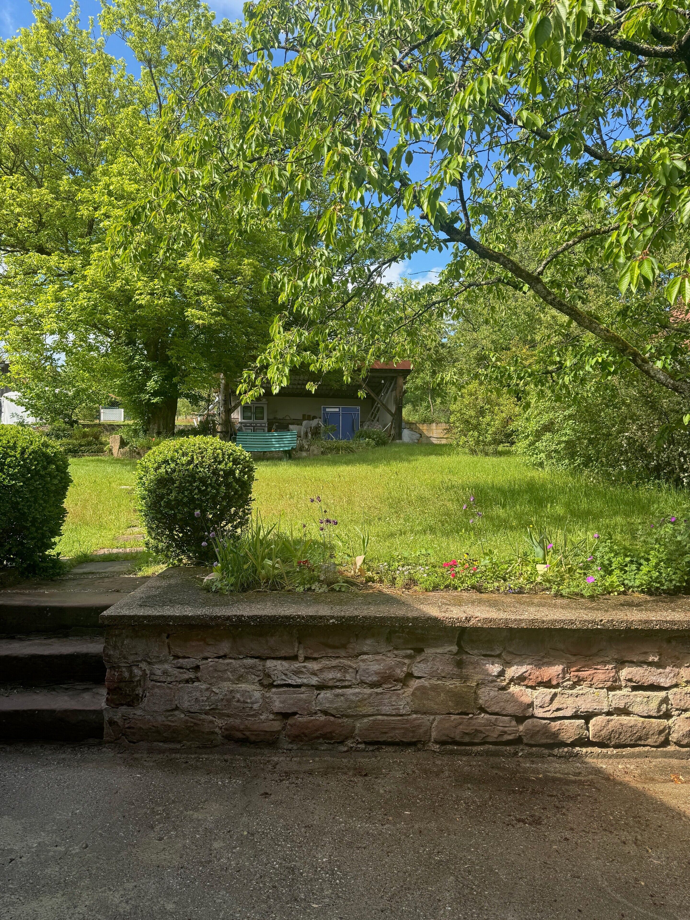 A stone wall, a grassy lawn, and a building with a blue door.