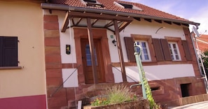 A building with a tiled roof, a wooden door, and a small garden area with plants.