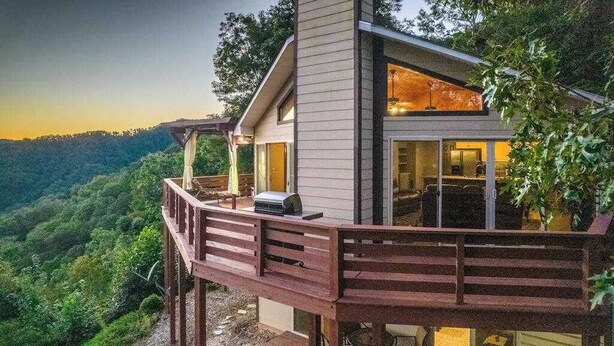 Una casa moderna amb terrassa, grans finestres i vista a una vall boscosa.