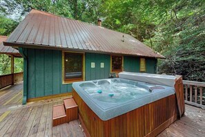 A wooden deck with a hot tub, a covered deck area, and a house with a metal roof.