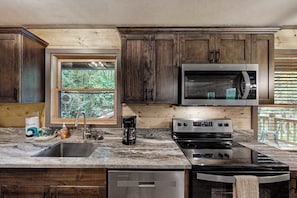 Una cocina con armarios de madera, un microondas de acero inoxidable, una estufa y una ventana con vistas al verdor.