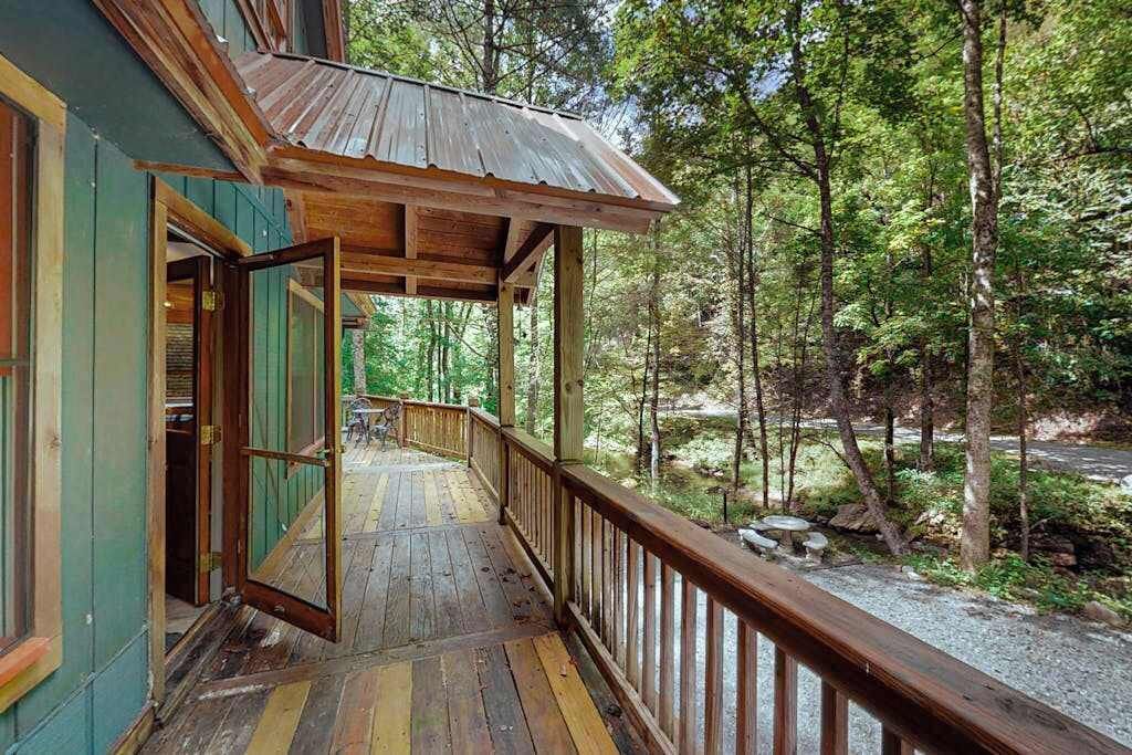 A wooden deck with a railing, leading to a building with green walls and a metal roof.