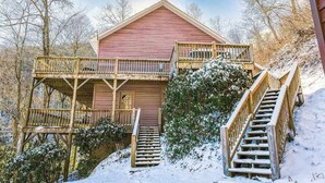 A wooden cabin with a balcony, a staircase, and a snow-covered landscape.