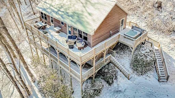 A wooden cabin with a deck, a hot tub, and a staircase leading to a second level.