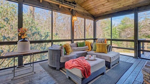 A covered outdoor seating area with a sofa, a table with a vase, and a bench.