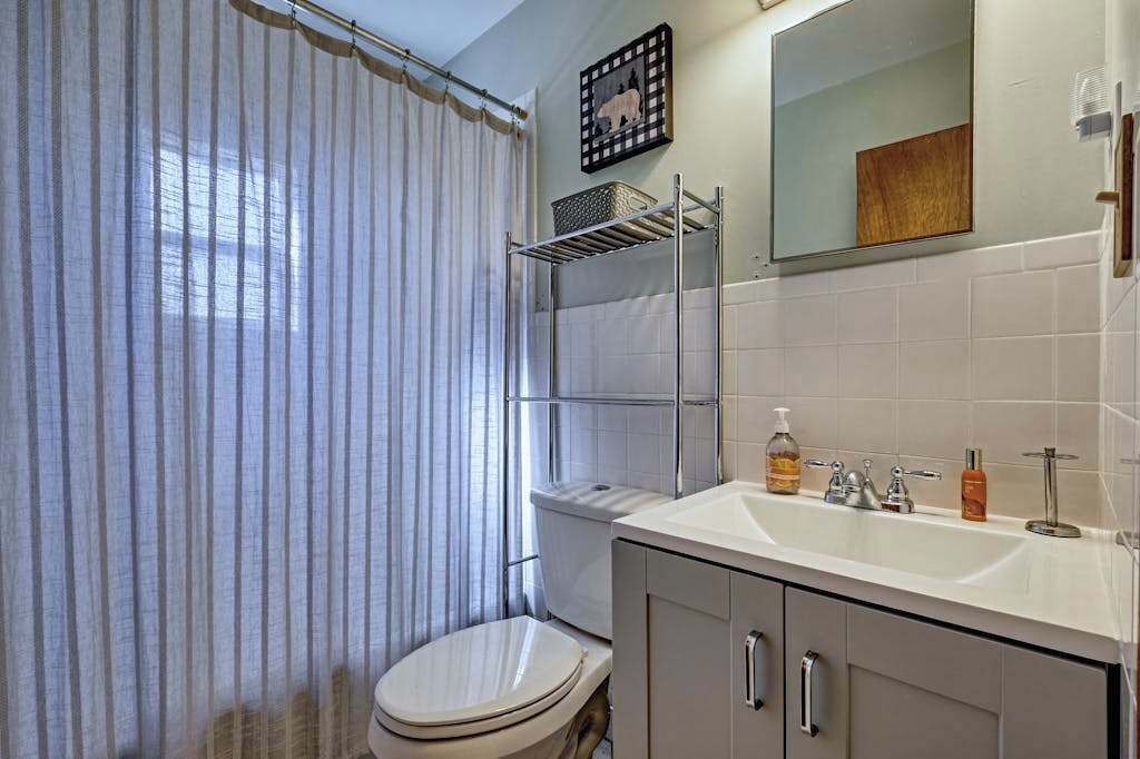 A bathroom with a toilet, a sink, a mirror, a shower curtain, and a shelf with toiletries.