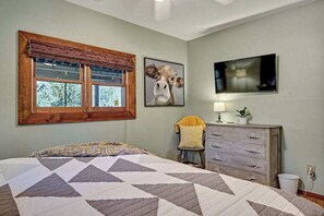 Un dormitorio con una cama grande, una ventana con persianas, un televisor montado en la pared, un aparador y una silla.