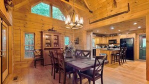 Interior de una caba ña de madera con comedor, cocina y ventanas amplias.