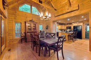 A wooden cabin interior with a dining area, kitchen, and large windows. - Glen Laurel Cabin (Cullowhee)