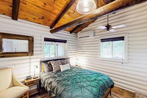 A log cabin bedroom with a bed, two windows, a ceiling fan, and a chair. - Mountain Dreams (Bryson City)