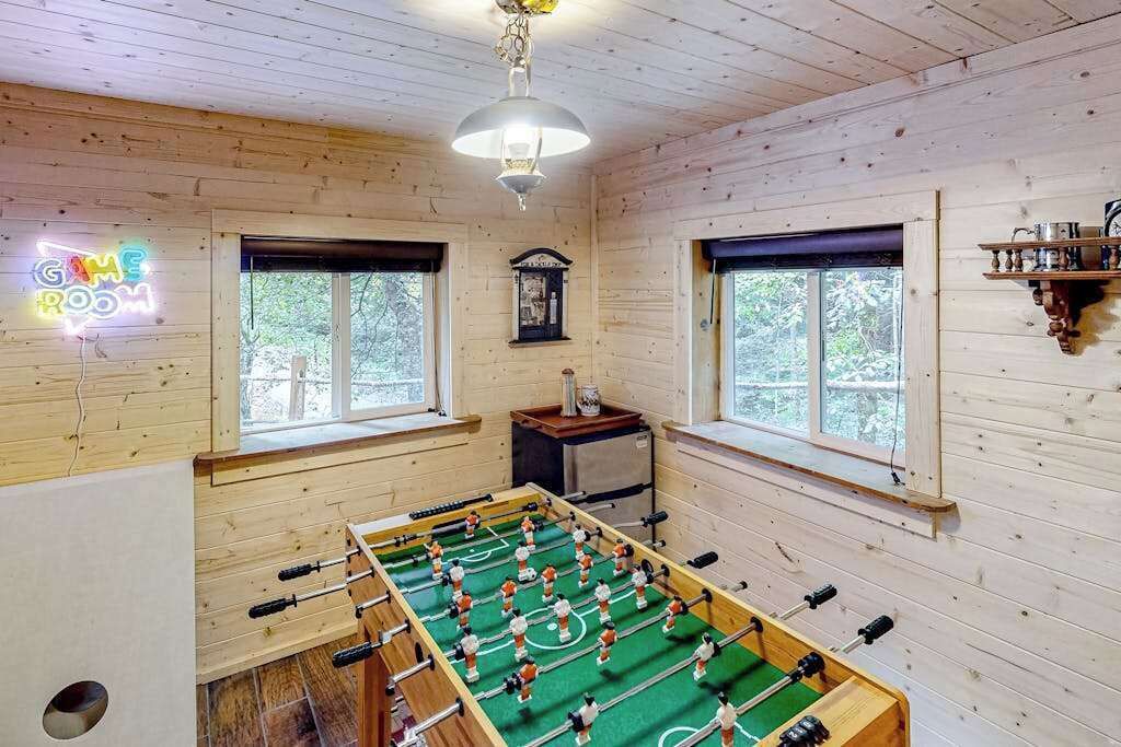 A room with wooden walls, a foosball table, a neon sign, and a clock.