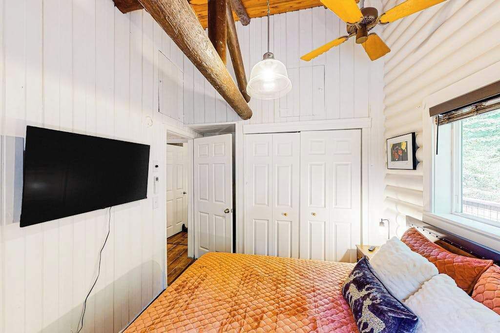 Ein Schlafzimmer mit Bett, Deckenventilator, an der Wand montiertem Fernseher und einem Fenster mit Blick.