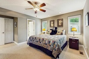 Ein Schlafzimmer mit einem Bett, einem Deckenventilator, einem Nachttisch und einem Fenster mit Jalousien.
