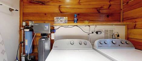 A laundry room with two Whirlpool washers, a water heater, and a shelf with a Black & Decker box.