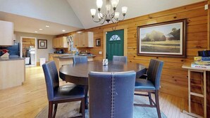 A dining area with a round table and chairs, wooden walls, a chandelier, and a green door. - Hawks Landing (Sylva)