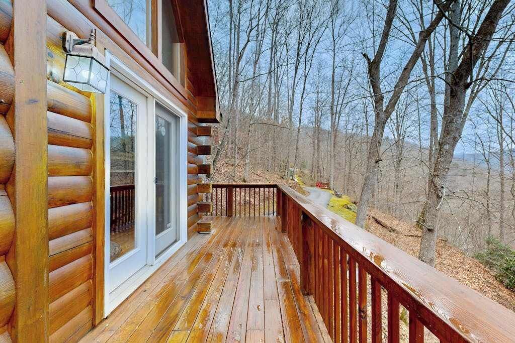 A wooden cabin with a deck, a glass door, and a view of a forested area.
