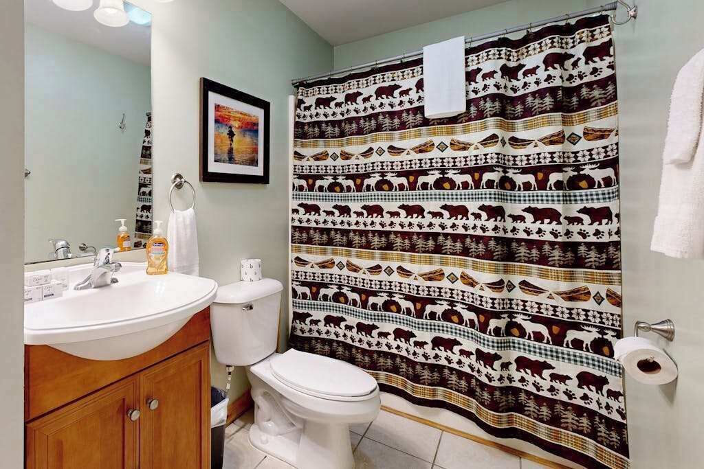 Une salle de bain avec un lavabo blanc, des toilettes et un rideau de douche orné de motifs animaliers.