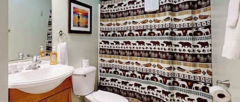 Une salle de bain avec un lavabo blanc, des toilettes et un rideau de douche orné de motifs animaliers.