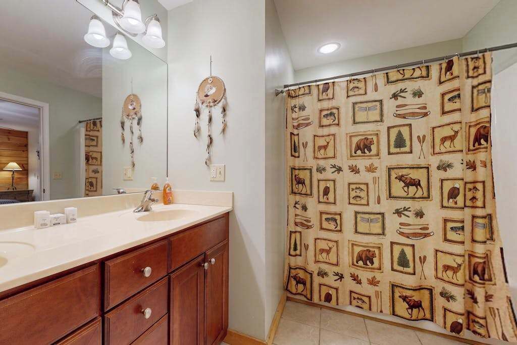 Une salle de bain avec un meuble-lavabo, un miroir, un rideau de douche à motifs animaliers et un attrape-rêves accroché au mur.