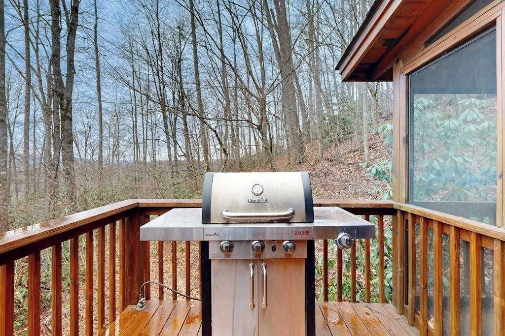 A barbecue grill on a wooden deck with a view of trees.