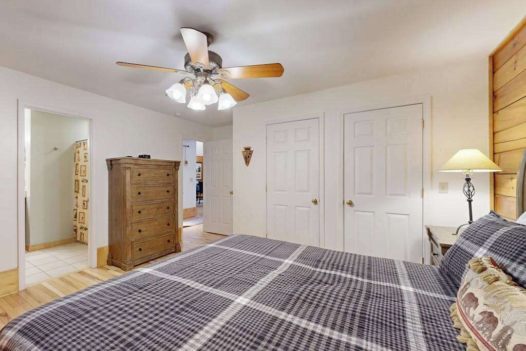 A bedroom with a bed, a ceiling fan, a dresser, and two doors.