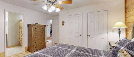 A bedroom with a bed, a ceiling fan, a dresser, and two doors.