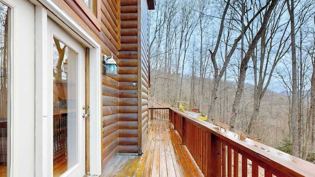 A wooden cabin with a deck, a glass door, and a view of a forest. - Hawks Landing (Sylva)