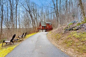 Ein Feldweg, der zu einer roten Holzhütte inmitten von Bäumen führt.