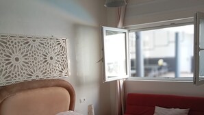 Een slaapkamer met een bed, een rode bank, een raam en een decoratief object aan de muur.