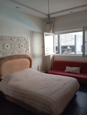 Ein Schlafzimmer mit einem Bett, einem roten Schlafsofa, einem Fenster und einer Wanddekoration.