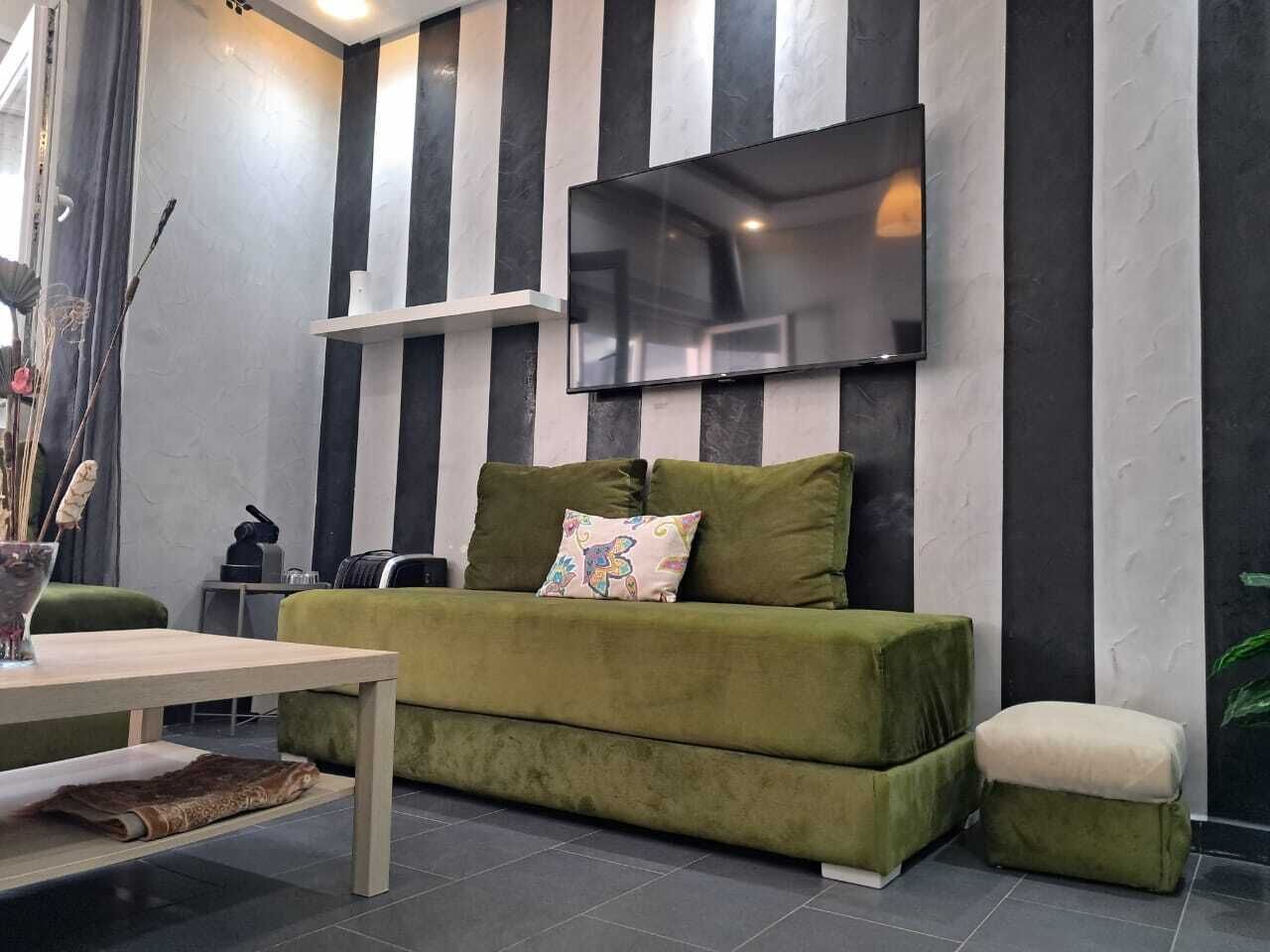 A modern living room with a sofa, a flat-screen TV mounted on the wall, a small table, and a decorative vase.