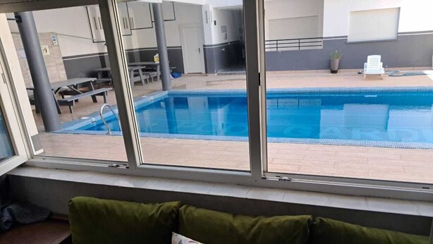 Een kamer met uitzicht op een zwembad, een raam en een groene, beklede bank met decoratief kussen.