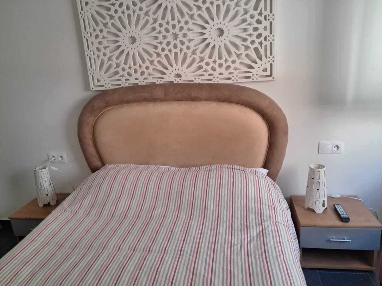 Un lit avec une couvre-lit à rayures, une tête de lit, des tables de chevet avec des lampes et un élément décoratif mural.