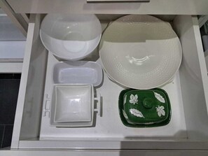 Eine Schublade mit verschiedenen Küchenutensilien, darunter Schüsseln, ein Teller, eine grüne Tablett mit Blumenmuster und ein rechteckiges Gefäß.