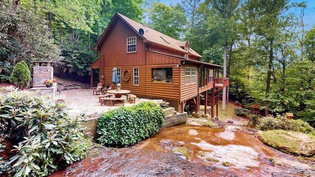 Una cabaña de madera con terraza, rodeada de exuberante vegetación y un arroyo.