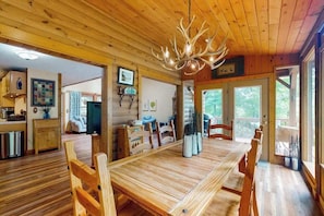 A wooden interior with a dining table, chairs, a chandelier, and a view through the door. - Misty Falls Hideaway (Cullowhee)