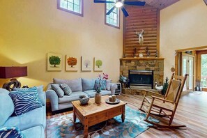 A cozy living room with a fireplace, a sofa, a coffee table, and a rocking chair. - Misty Falls Hideaway (Cullowhee)