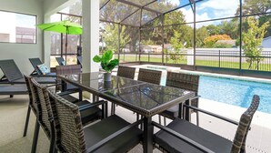 Une terrasse fermée par des baies vitrées, avec une piscine, des meubles en osier et un parasol vert.